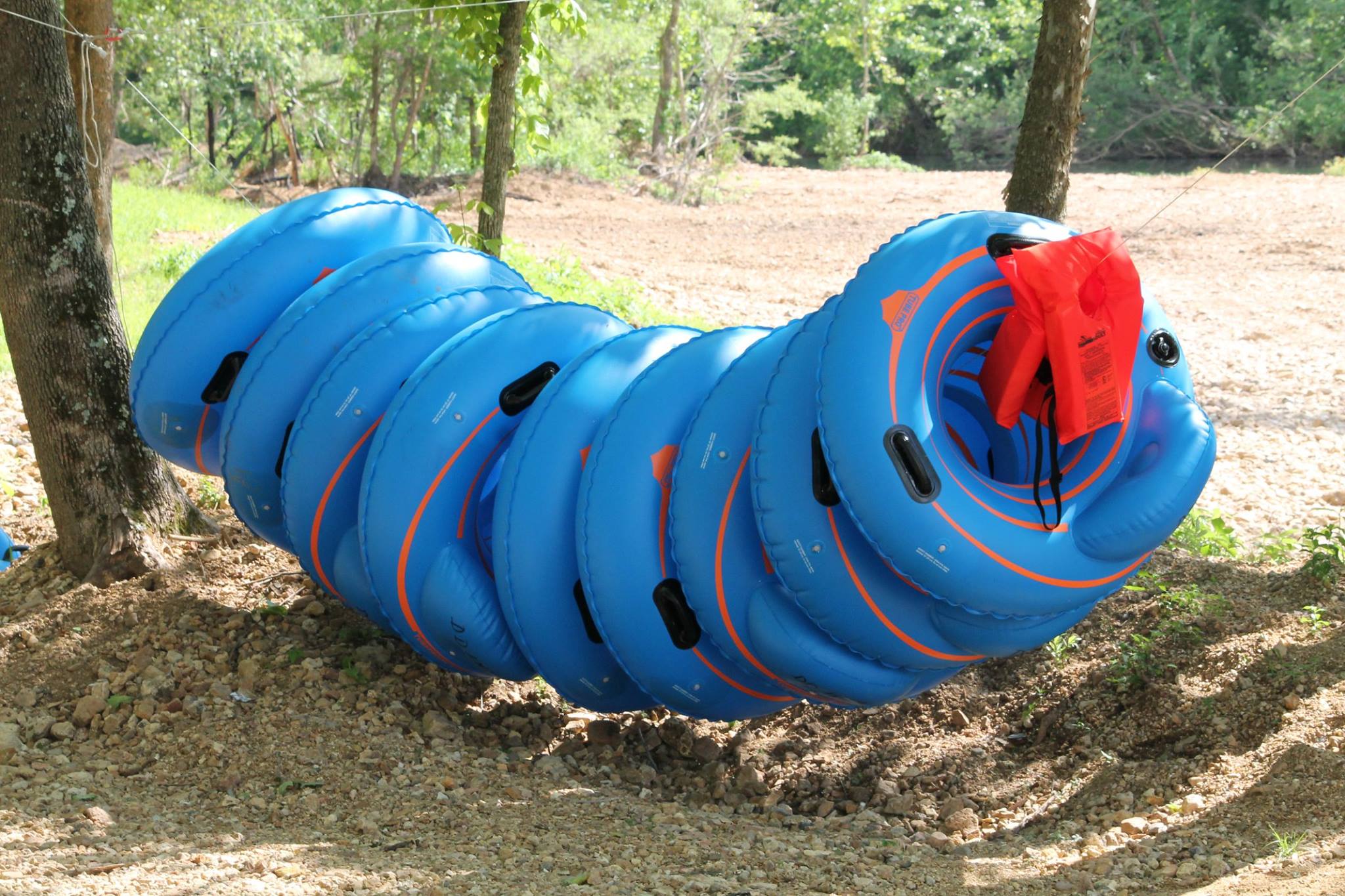 a collection of 13 blue innertube floating devices on a gravel beach area